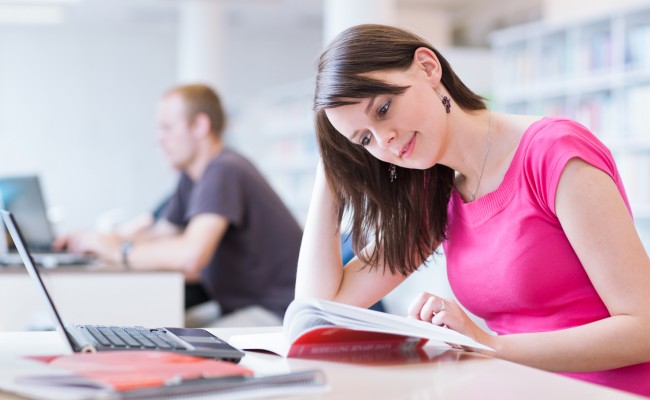 In the library – pretty female student with laptop and books